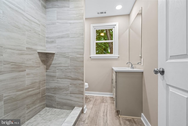 bathroom featuring hardwood / wood-style flooring, vanity, toilet, and a tile shower