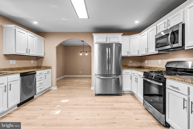 kitchen with light hardwood / wood-style flooring, white cabinets, dark stone counters, and appliances with stainless steel finishes