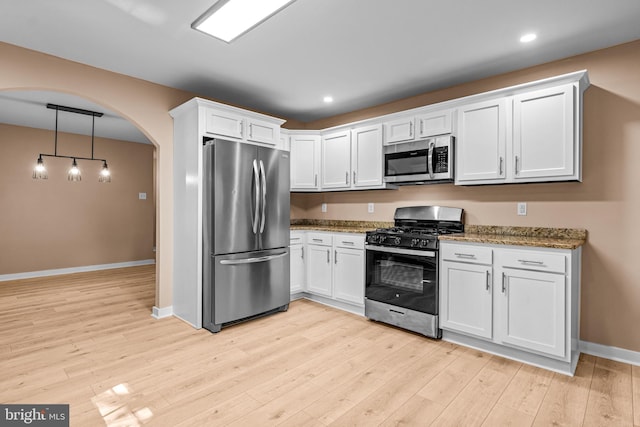 kitchen featuring appliances with stainless steel finishes, light wood-type flooring, pendant lighting, stone countertops, and white cabinetry