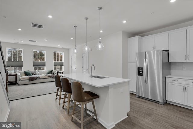 kitchen featuring stainless steel refrigerator with ice dispenser, sink, white cabinets, and a kitchen island with sink