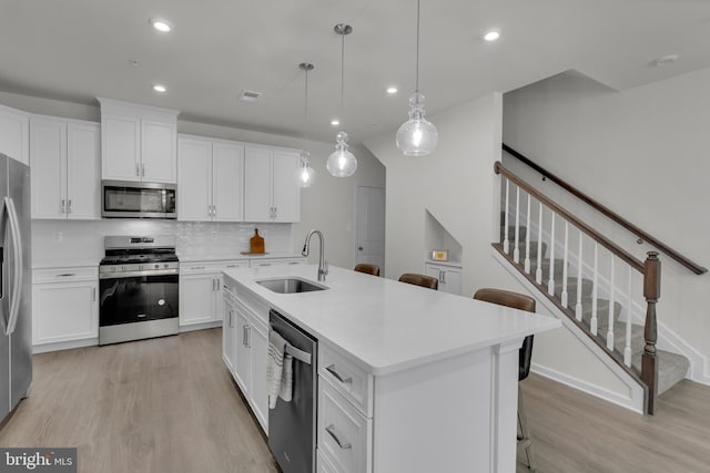 kitchen with pendant lighting, sink, white cabinetry, a kitchen island with sink, and appliances with stainless steel finishes