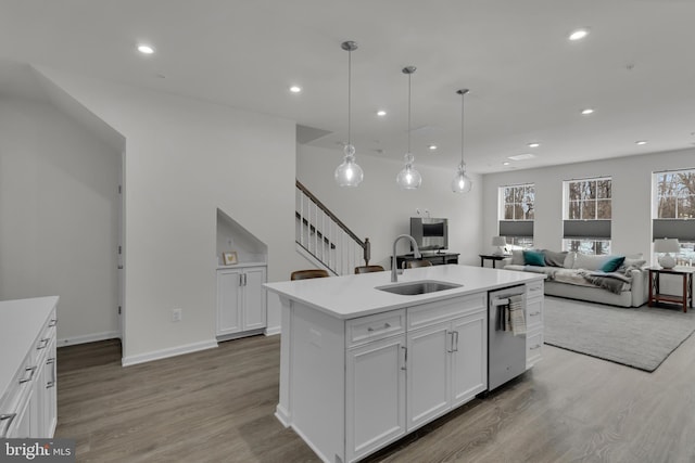 kitchen with decorative light fixtures, a center island with sink, stainless steel dishwasher, sink, and white cabinetry