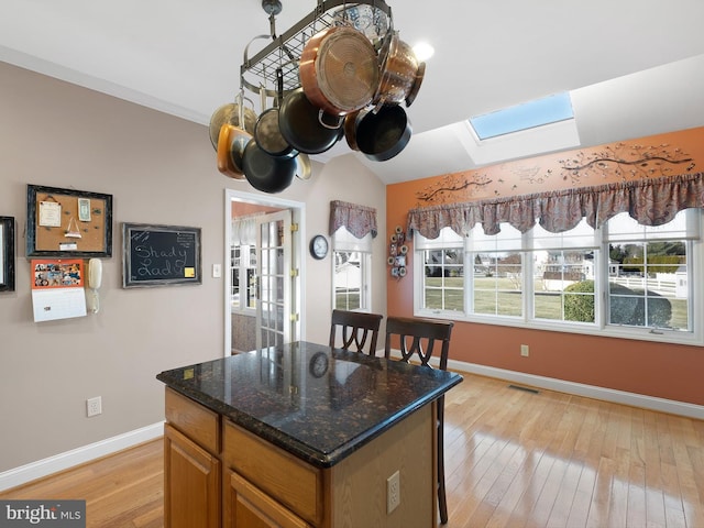 kitchen with dark stone countertops, vaulted ceiling with skylight, light hardwood / wood-style floors, and a center island