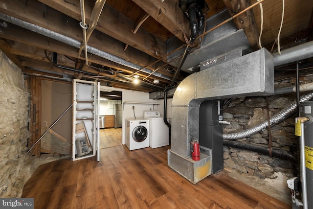 basement featuring hardwood / wood-style flooring, gas water heater, washing machine and clothes dryer, and stainless steel refrigerator