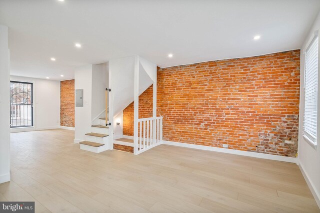 unfurnished room featuring brick wall, electric panel, and light hardwood / wood-style floors