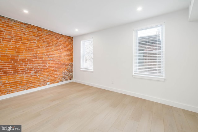 empty room with brick wall, plenty of natural light, and light hardwood / wood-style floors