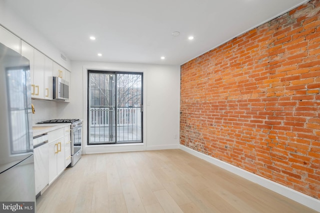 kitchen featuring brick wall, light hardwood / wood-style floors, white cabinets, and appliances with stainless steel finishes