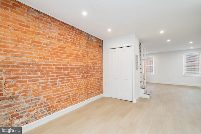 basement featuring brick wall and light hardwood / wood-style flooring