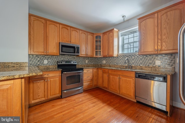 kitchen featuring light stone countertops, appliances with stainless steel finishes, tasteful backsplash, sink, and light hardwood / wood-style flooring