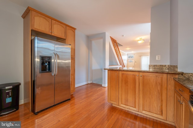 kitchen featuring stainless steel fridge with ice dispenser, kitchen peninsula, stone countertops, and light wood-type flooring