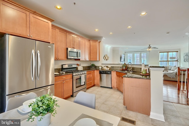 kitchen featuring dark stone countertops, stainless steel appliances, kitchen peninsula, ceiling fan, and sink