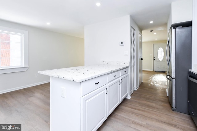 kitchen with stainless steel refrigerator, white cabinetry, light stone countertops, and light wood-type flooring