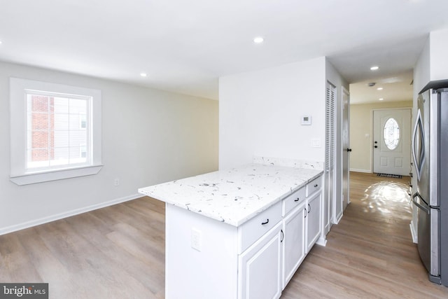 kitchen with white cabinets, light hardwood / wood-style floors, light stone counters, and stainless steel refrigerator