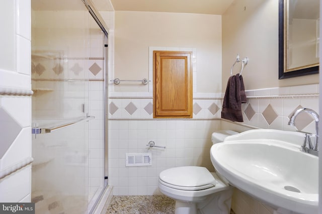 bathroom featuring sink, a shower with shower door, tile walls, and toilet