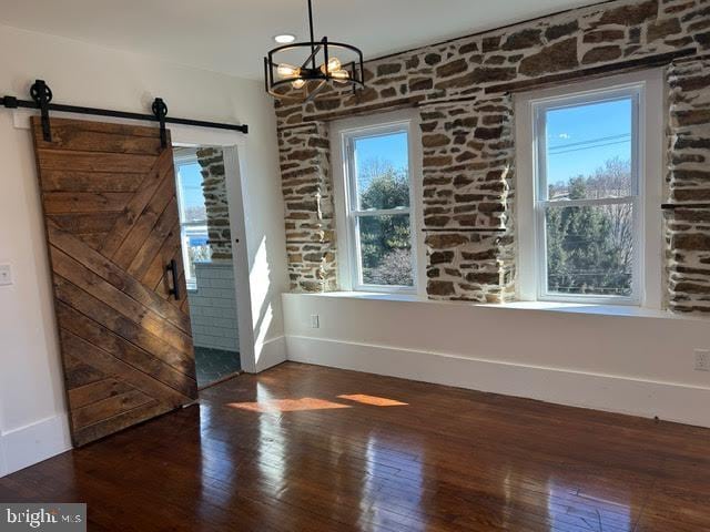 unfurnished dining area featuring dark wood-style floors, a barn door, and a notable chandelier