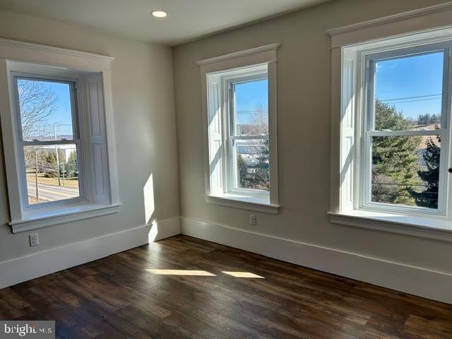 spare room with dark wood-style flooring, a wealth of natural light, and baseboards