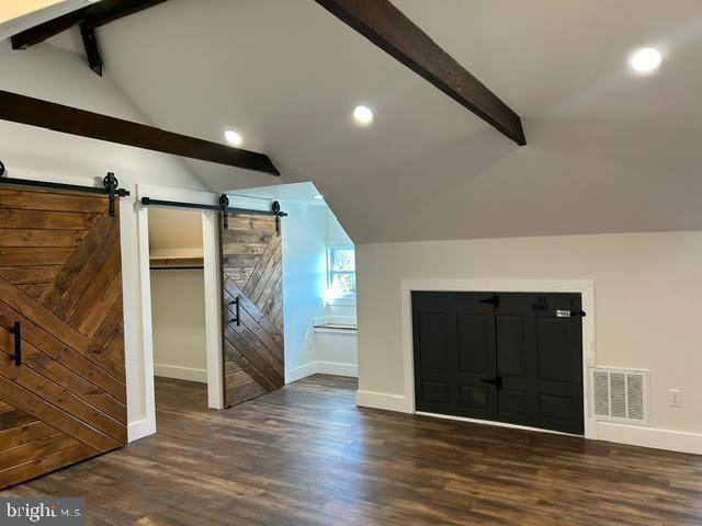 bonus room with visible vents, lofted ceiling with beams, a barn door, dark wood-type flooring, and baseboards