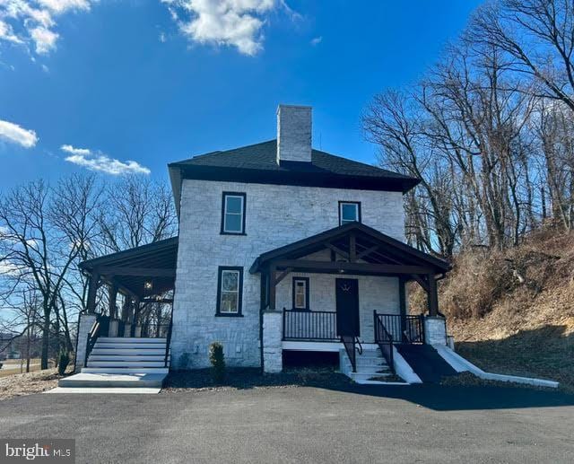 american foursquare style home featuring stone siding, a porch, and a chimney