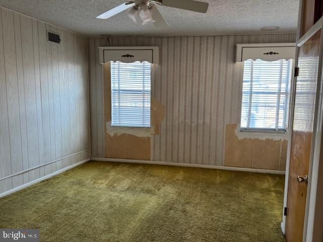 carpeted spare room with ceiling fan, a textured ceiling, and wood walls