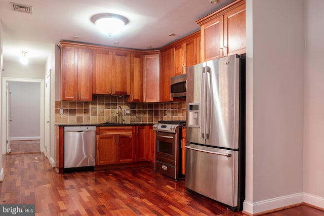 kitchen featuring appliances with stainless steel finishes, tasteful backsplash, sink, dark stone countertops, and dark hardwood / wood-style floors