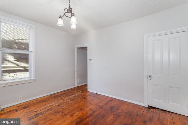 empty room featuring a textured ceiling, dark wood-type flooring, and a chandelier