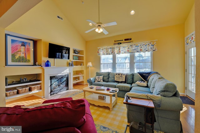 living room featuring built in shelves, light hardwood / wood-style flooring, high vaulted ceiling, and ceiling fan