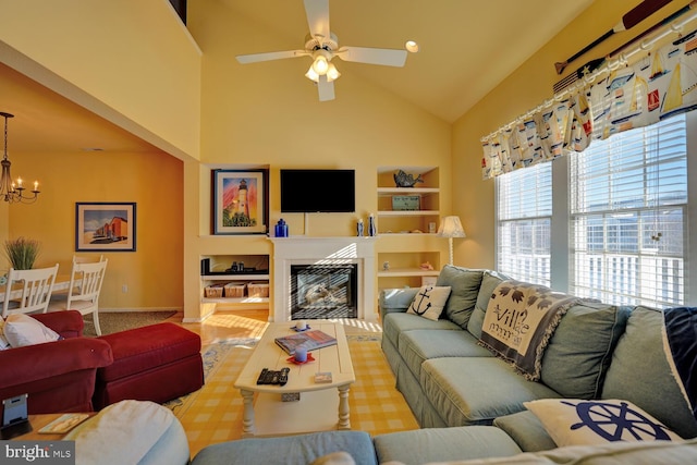 living room featuring built in shelves, ceiling fan with notable chandelier, and high vaulted ceiling