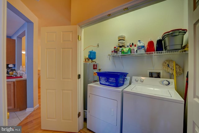 laundry room with light wood-type flooring, washing machine and dryer, and water heater