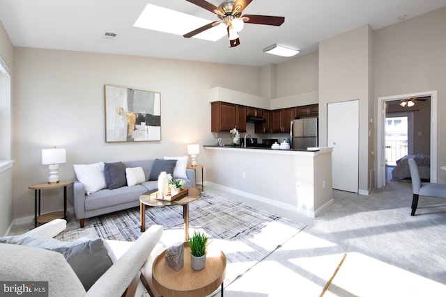 carpeted living room with high vaulted ceiling, ceiling fan, and a skylight