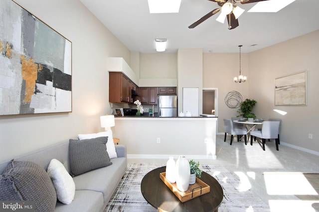 living room with a towering ceiling, a skylight, ceiling fan with notable chandelier, and light carpet