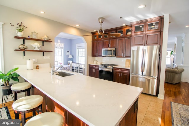 kitchen with kitchen peninsula, appliances with stainless steel finishes, a kitchen breakfast bar, sink, and light tile patterned floors