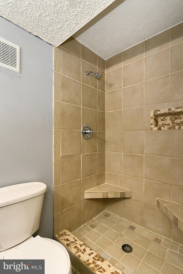 bathroom with toilet, a textured ceiling, and a tile shower