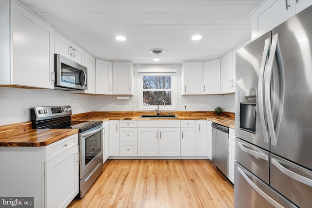 kitchen with appliances with stainless steel finishes, light wood-type flooring, wood counters, white cabinets, and sink