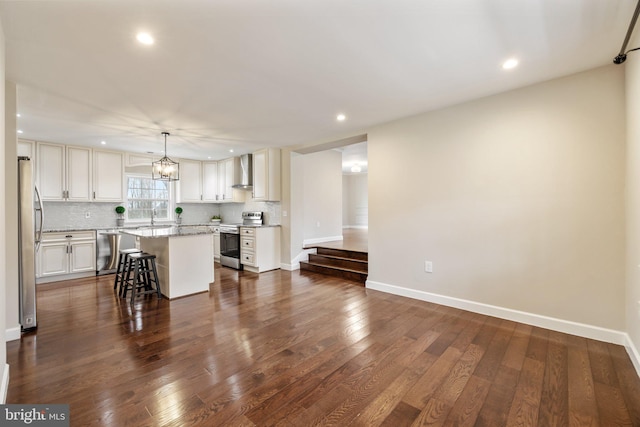 kitchen featuring dark wood-type flooring, backsplash, a kitchen island, appliances with stainless steel finishes, and wall chimney exhaust hood