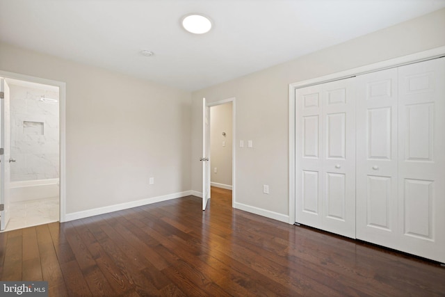 unfurnished bedroom featuring a closet, ensuite bathroom, baseboards, and wood-type flooring