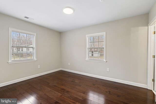 empty room featuring dark wood-type flooring, visible vents, and baseboards