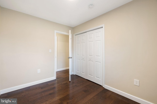 unfurnished bedroom featuring baseboards, dark wood-style flooring, and a closet