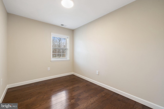 unfurnished room with dark wood-style floors, visible vents, and baseboards