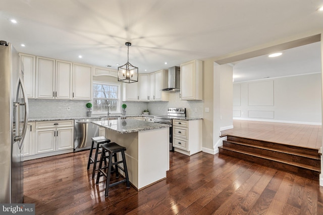 kitchen featuring light stone counters, dark wood-style flooring, stainless steel appliances, wall chimney range hood, and a center island