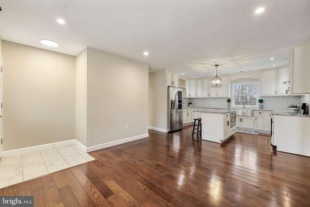 kitchen featuring dark wood finished floors, a breakfast bar, stainless steel fridge, backsplash, and a center island