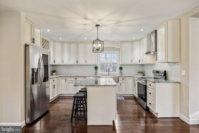 kitchen with dark wood-style floors, a center island, appliances with stainless steel finishes, wall chimney exhaust hood, and light stone countertops