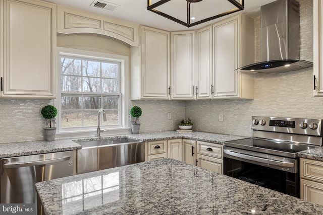 kitchen with cream cabinets, appliances with stainless steel finishes, and wall chimney range hood