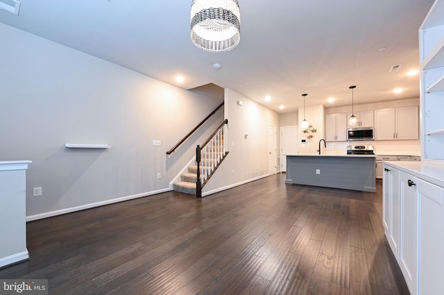 kitchen with white cabinets, stainless steel appliances, sink, hanging light fixtures, and a kitchen island with sink