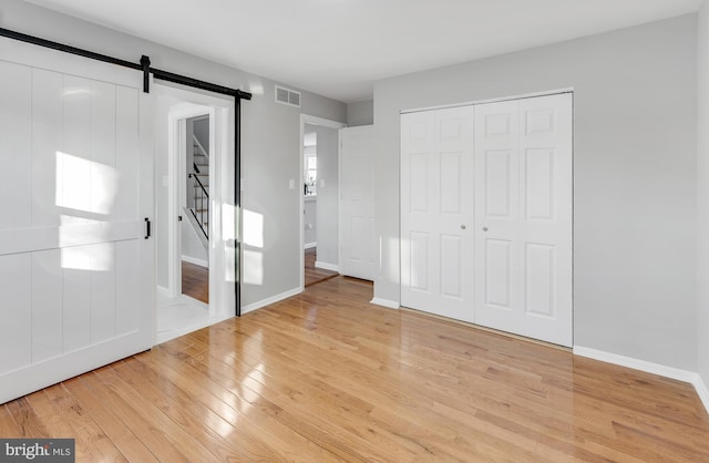 unfurnished bedroom with a closet, light hardwood / wood-style floors, and a barn door