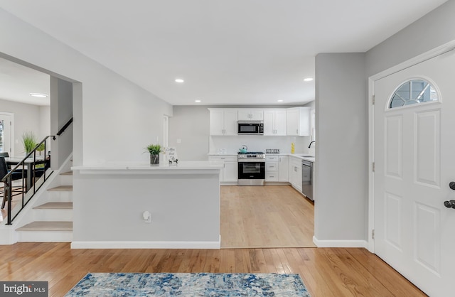 kitchen featuring kitchen peninsula, stainless steel appliances, white cabinets, light hardwood / wood-style flooring, and sink