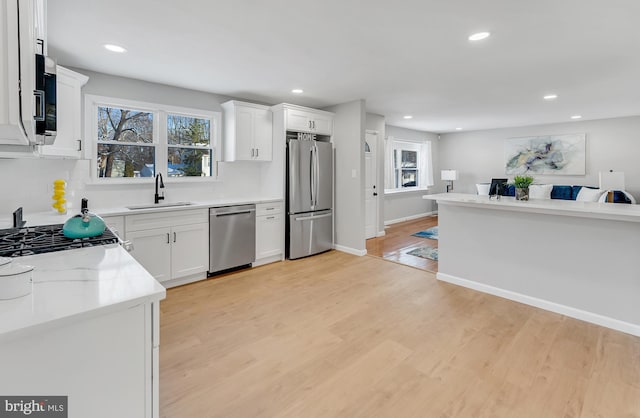 kitchen featuring white cabinets, appliances with stainless steel finishes, light hardwood / wood-style floors, sink, and light stone counters