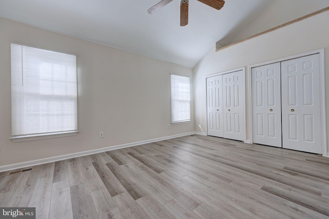 unfurnished bedroom featuring ceiling fan, multiple windows, light hardwood / wood-style flooring, and multiple closets