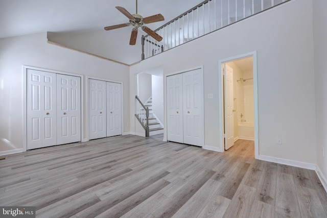 unfurnished bedroom featuring a high ceiling, connected bathroom, ceiling fan, light hardwood / wood-style flooring, and multiple closets