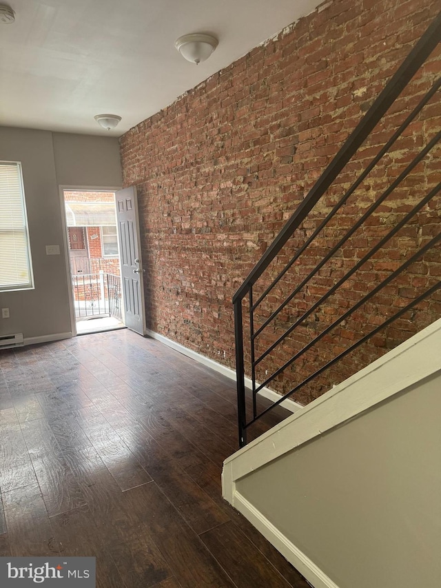 unfurnished room with dark hardwood / wood-style flooring, brick wall, and a baseboard heating unit