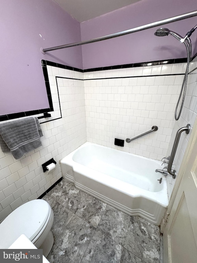 bathroom with tiled shower / bath combo, toilet, and tile walls